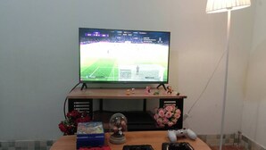 Een houten tafel met een televisie, gamecontrollers, een bloemstuk en een kleine verzameling beeldjes.