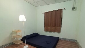 Een kleine kamer met een enkel bed, houten vloer, nachtkastje, lamp en raam met bruine gordijnen.