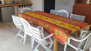 Ein Essbereich mit einem Tisch, der mit einer gemusterten Tischdecke bedeckt ist, umgeben von weißen Stühlen.