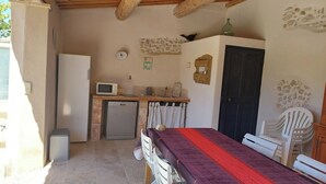 Eine kompakte Küche mit Mikrowelle, Kühlschrank und Spüle. Es gibt einen Essbereich mit Tisch und Stühlen sowie eine kleine Sitzecke mit einem Sessel und einer Bank.