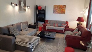 Ein Wohnzimmer mit einem Ecksofa, einem roten Sessel, einem Couchtisch und einem Bücherregal.
