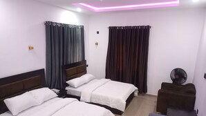Quarto de hotel com duas camas, um pequeno sofá, um ventilador e cortinas.