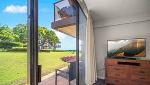 Ein Zimmer mit einer großen Schiebeglasdoor, die auf eine Terrasse mit einem Stuhl und Blick auf eine Rasenfläche sowie ein Gebäude führt. Es befindet sich ein Holzschrank mit einem Flachbildfernseher darauf.