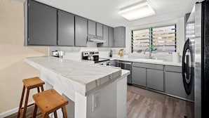 Eine moderne Küche mit grauen Schränken, einer weißen Arbeitsplatte, einem Edelstahlkühlschrank und einem Fenster mit Blick auf ein Geschäft.