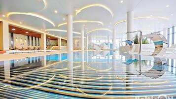 Una amplia piscina interior con diseño moderno, que cuenta con una isla central y zonas de estar a lo largo de los bordes.