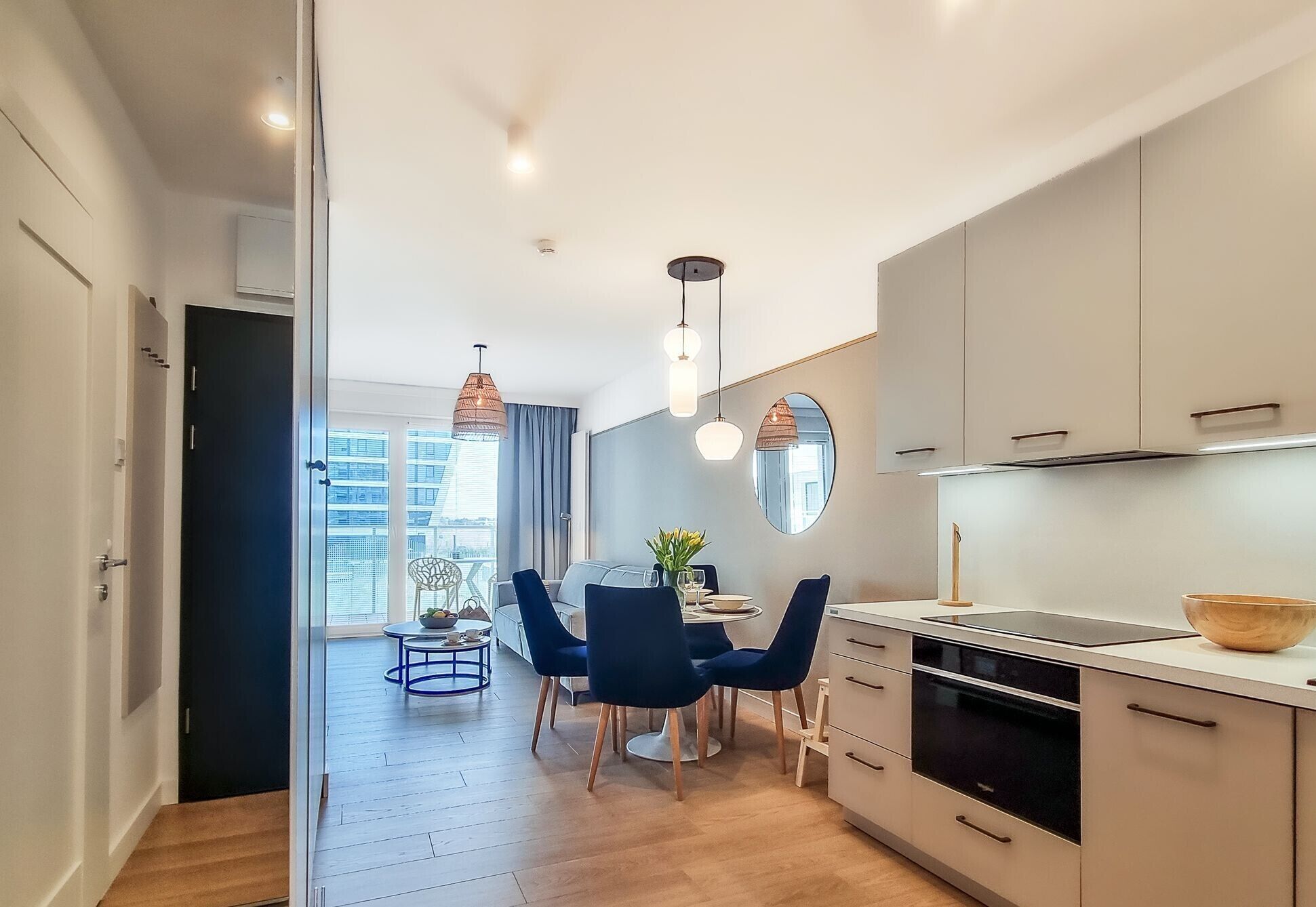 A modern kitchen with a dining area, featuring a large window, pendant lights, and a view of the cityscape.