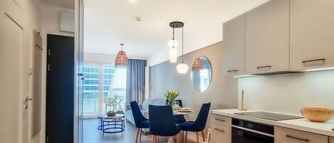 A modern kitchen with a dining area, featuring a large window, pendant lights, and a view of the cityscape.