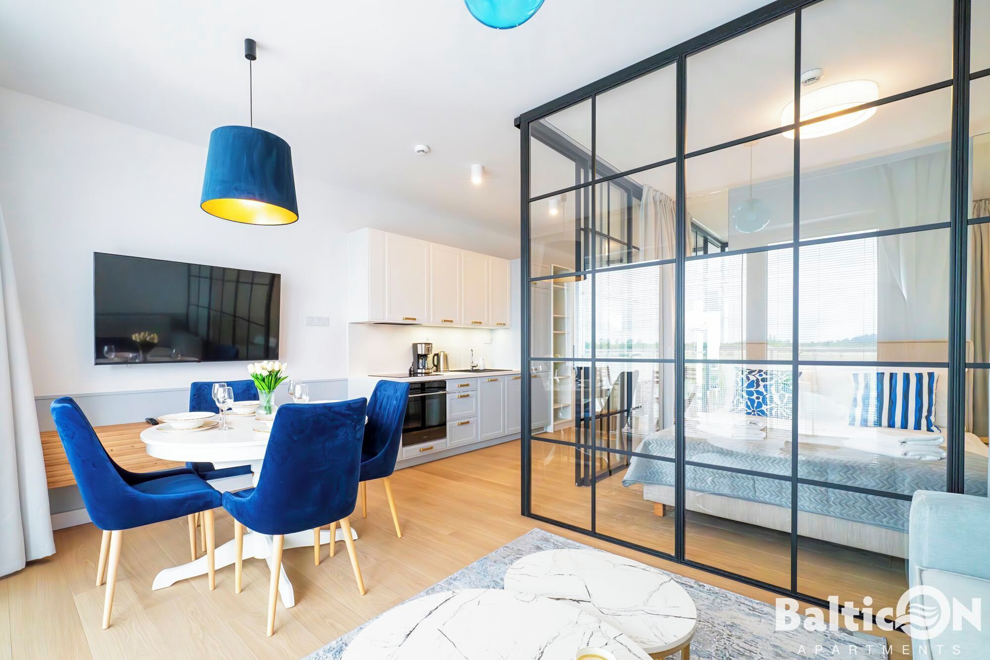 A modern apartment with a dining area, kitchen, and a large glass sliding door leading to a balcony.