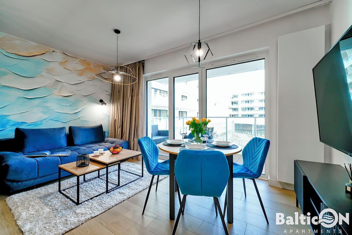 Un soggiorno moderno con un divano blu, un tavolo da pranzo con sedie, un'ampia finestra vista edifici e una televisione a schermo piatto.