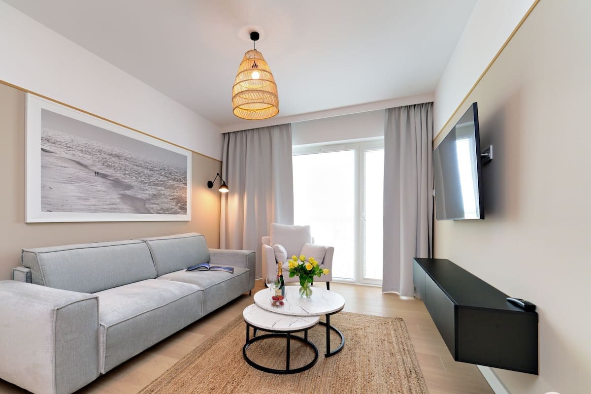 Un soggiorno moderno con un divano grigio, un tavolino rotondo, un quadro grande, una televisione a schermo piatto e un lampadario.