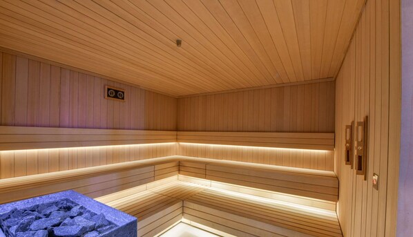 Una sauna con paredes y bancos de madera, una pila de piedra y una pequeña placa en la pared.