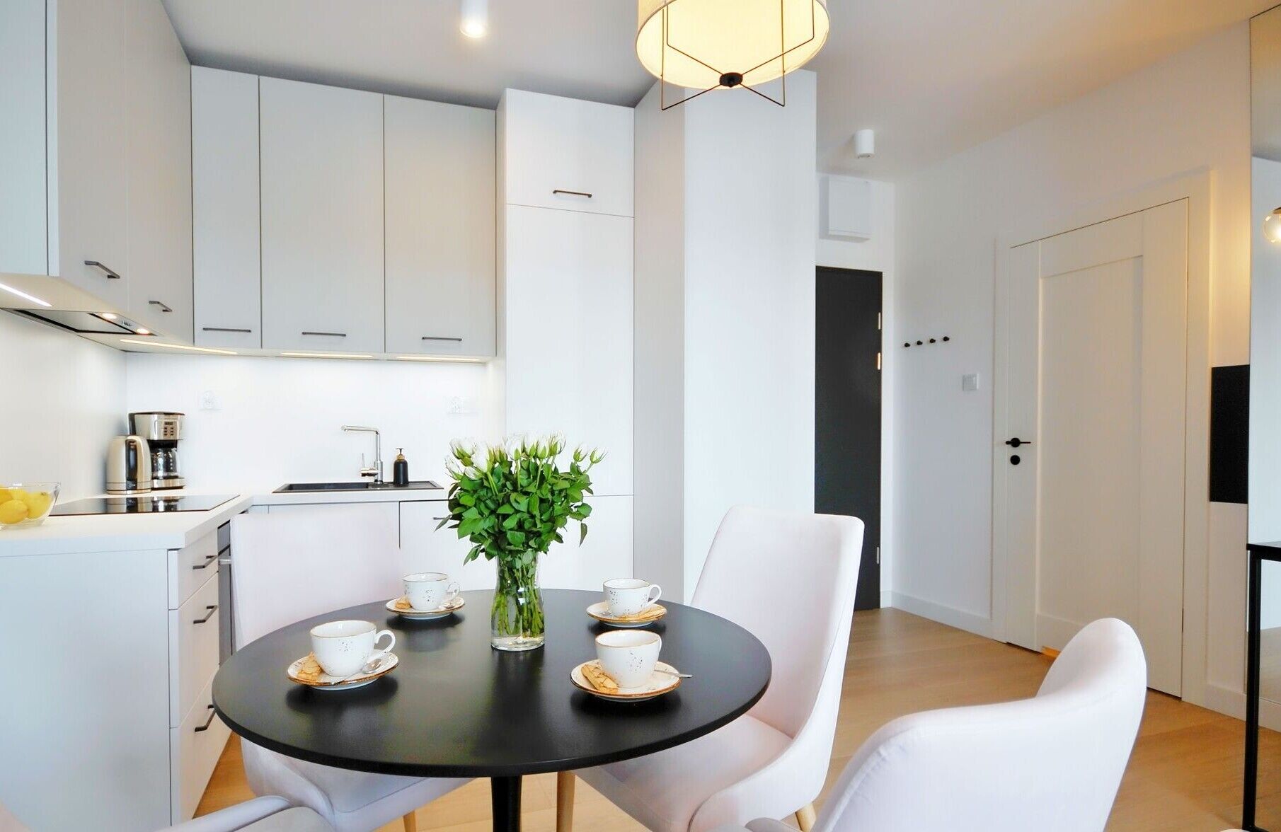 Una cocina moderna con armarios blancos, una cafetera y un comedor con una mesa redonda y sillas blancas.
