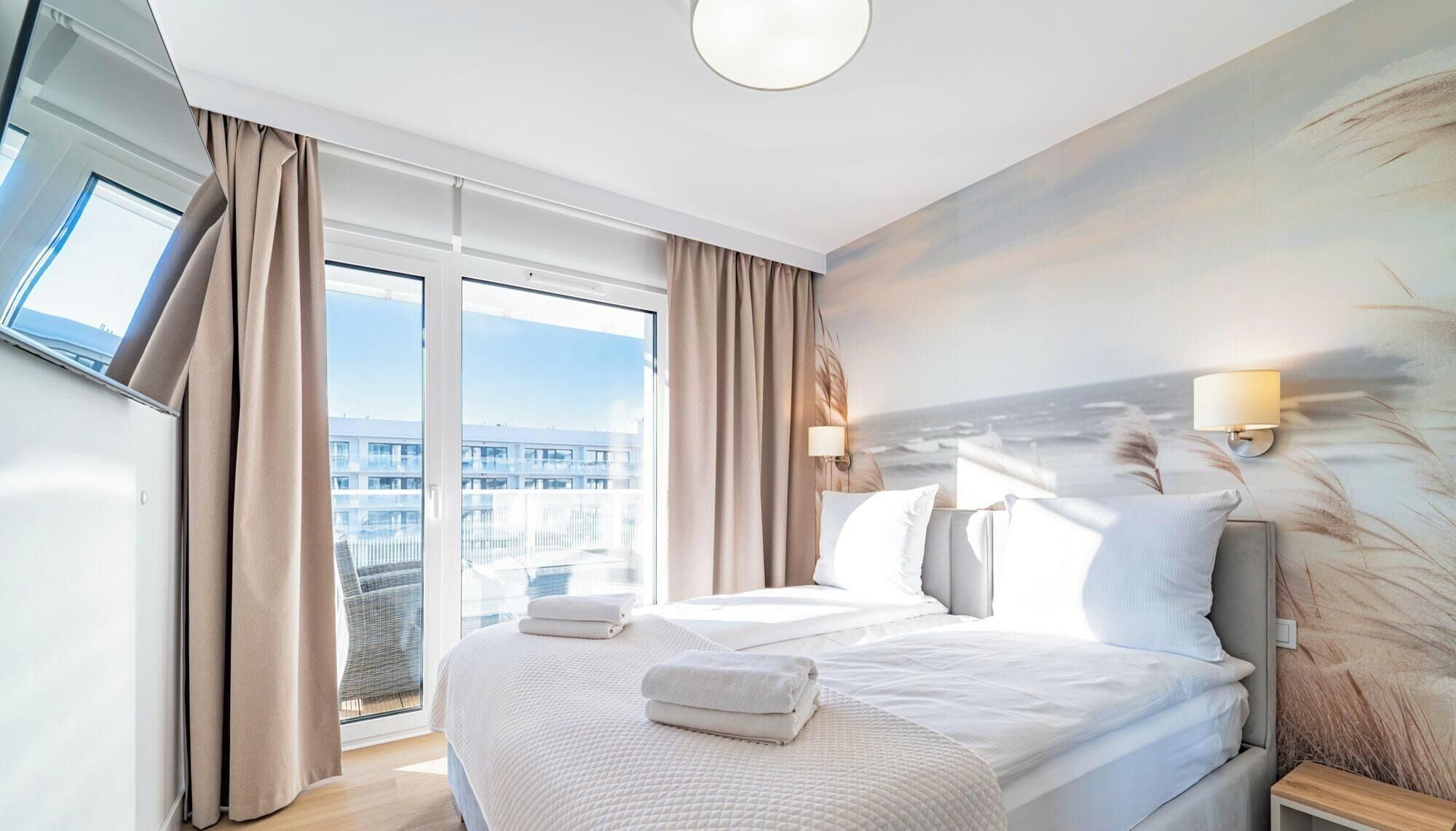 Habitación de hotel moderna con una cama grande, dos lámparas de noche, vistas de la ciudad a través de ventanales del suelo al techo y un cuadro en la pared.