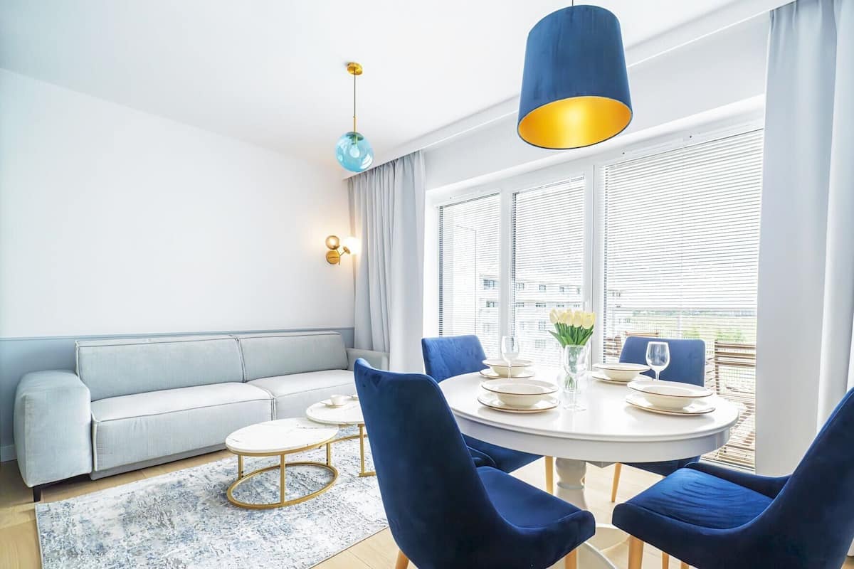 Un soggiorno moderno con un tavolo da pranzo rotondo, sedie blu, un divano grigio chiaro e una lampada a sospensione blu.