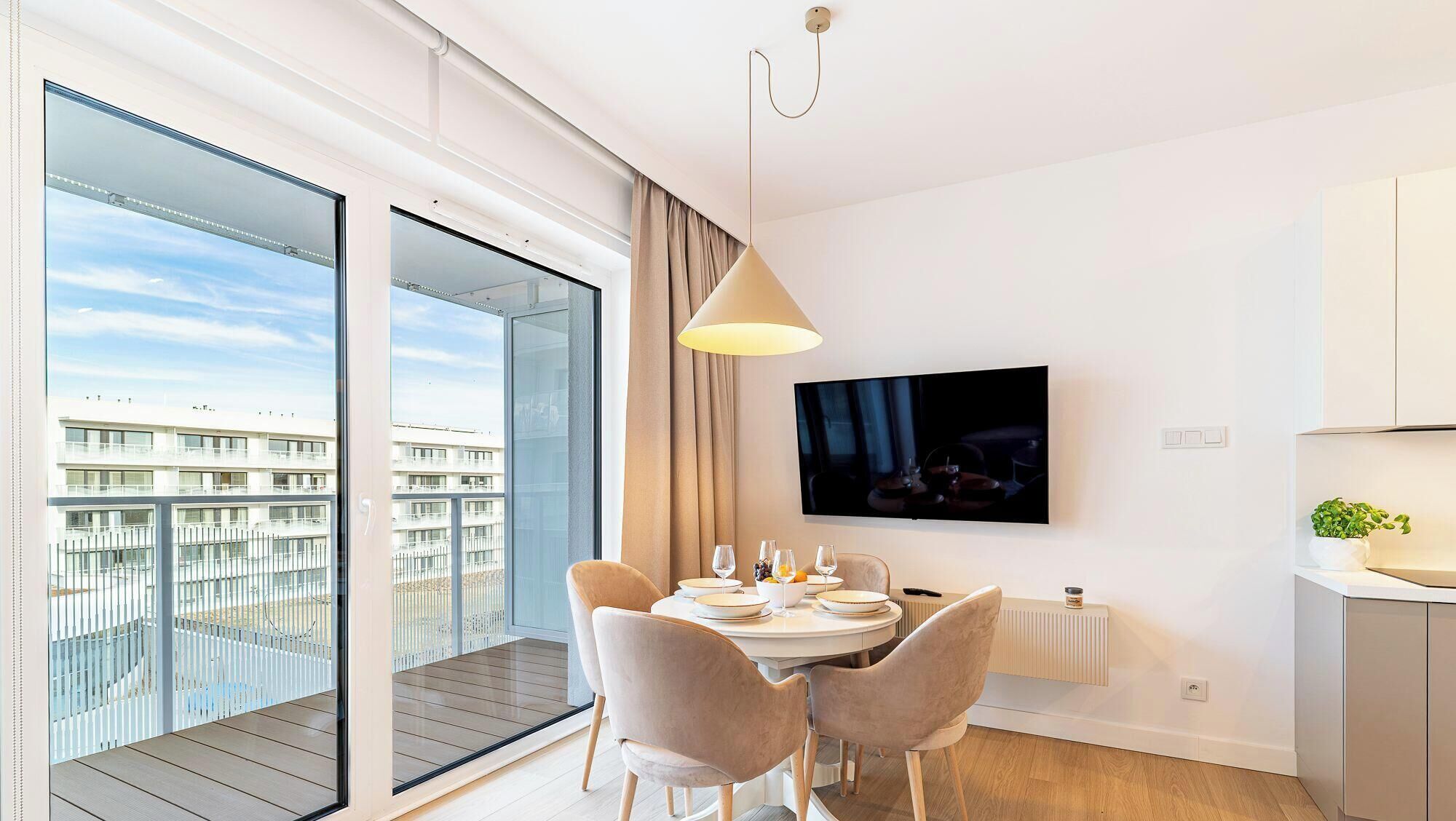 A modern living room with a dining area, a TV mounted on the wall, and a view of a building through large windows.