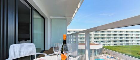Un balcon avec une table, deux chaises, une bouteille de vin rosé, deux verres, un saladier de fraises et un magazine.
