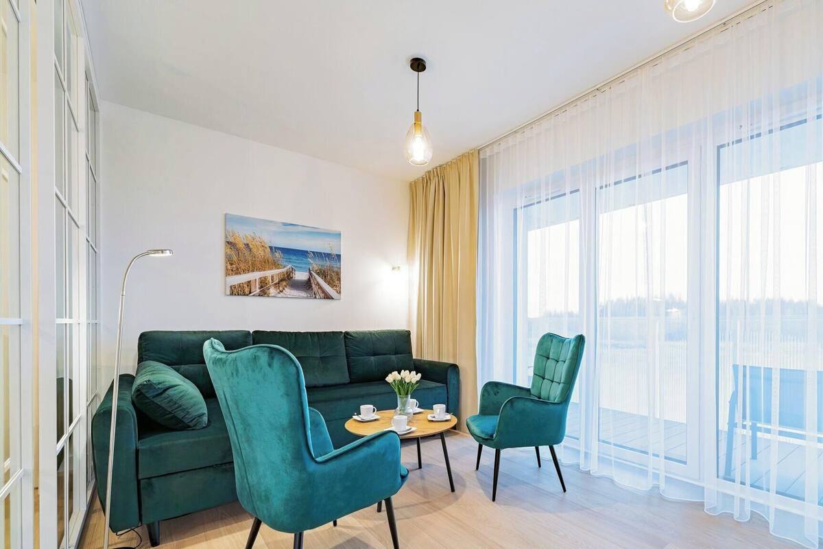 Un soggiorno moderno con un divano verde, due poltrone abbinate, un tavolino rotondo con una tazza e un piattino, e un quadro raffigurante una spiaggia.