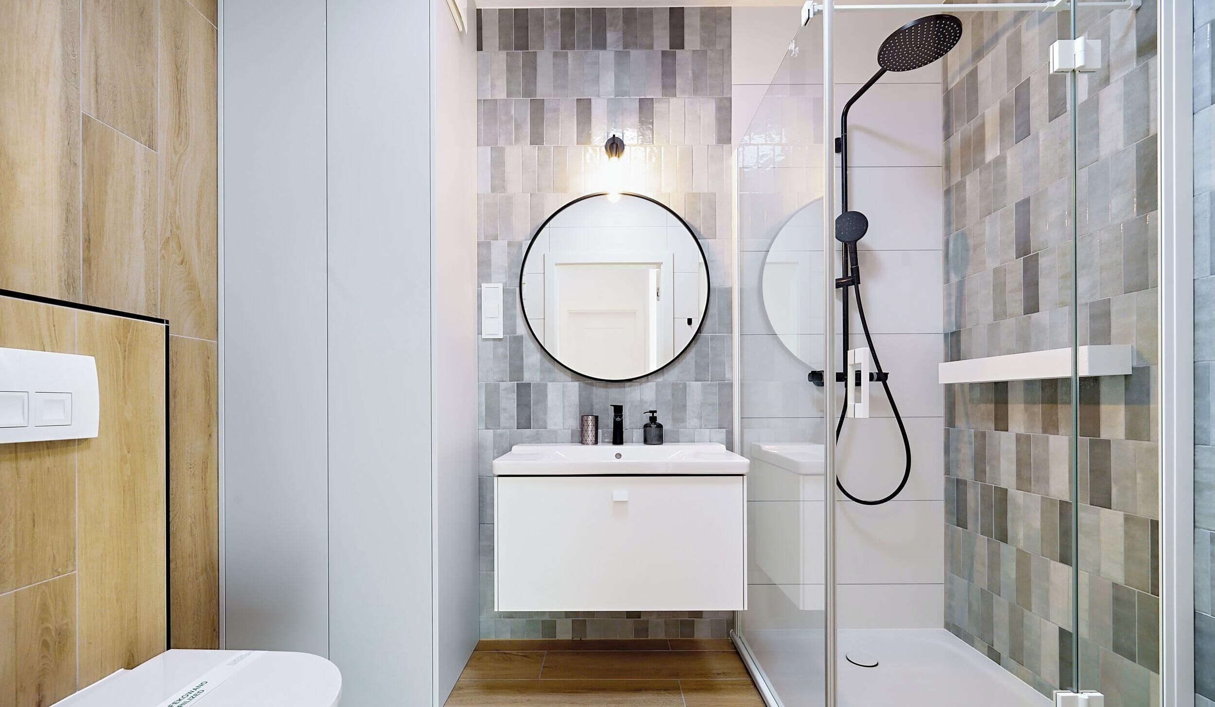 A modern bathroom with a glass shower enclosure, a round mirror, and a white vanity.