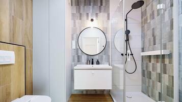 A modern bathroom with a glass shower enclosure, a round mirror, and a white vanity.