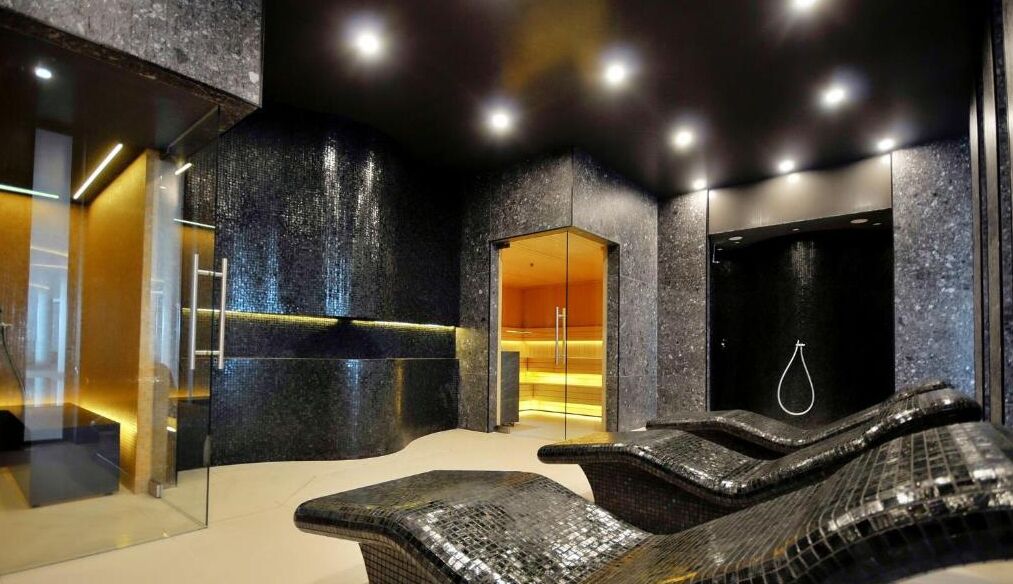A spa area with a massage chair, a glass-enclosed shower, and a dark-toned wall with a textured finish.