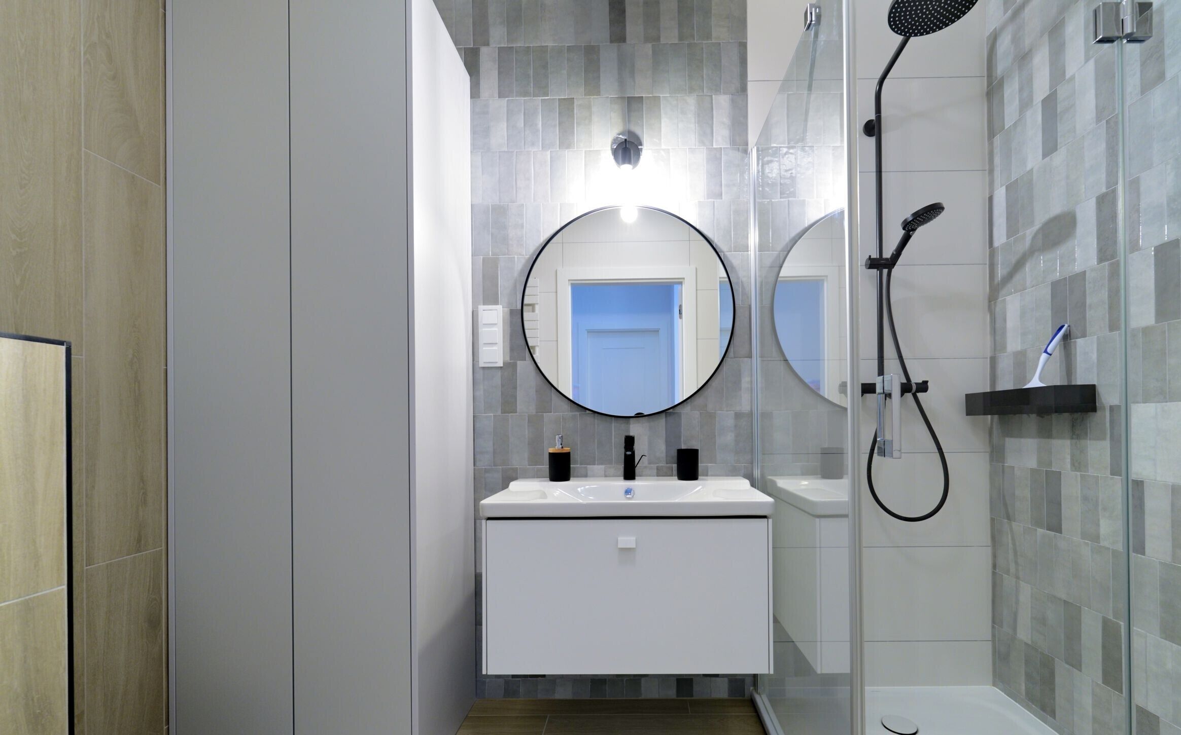 Een moderne badkamer met een douchecabine van glas, een ronde spiegel en een witte wastafelmeubel.