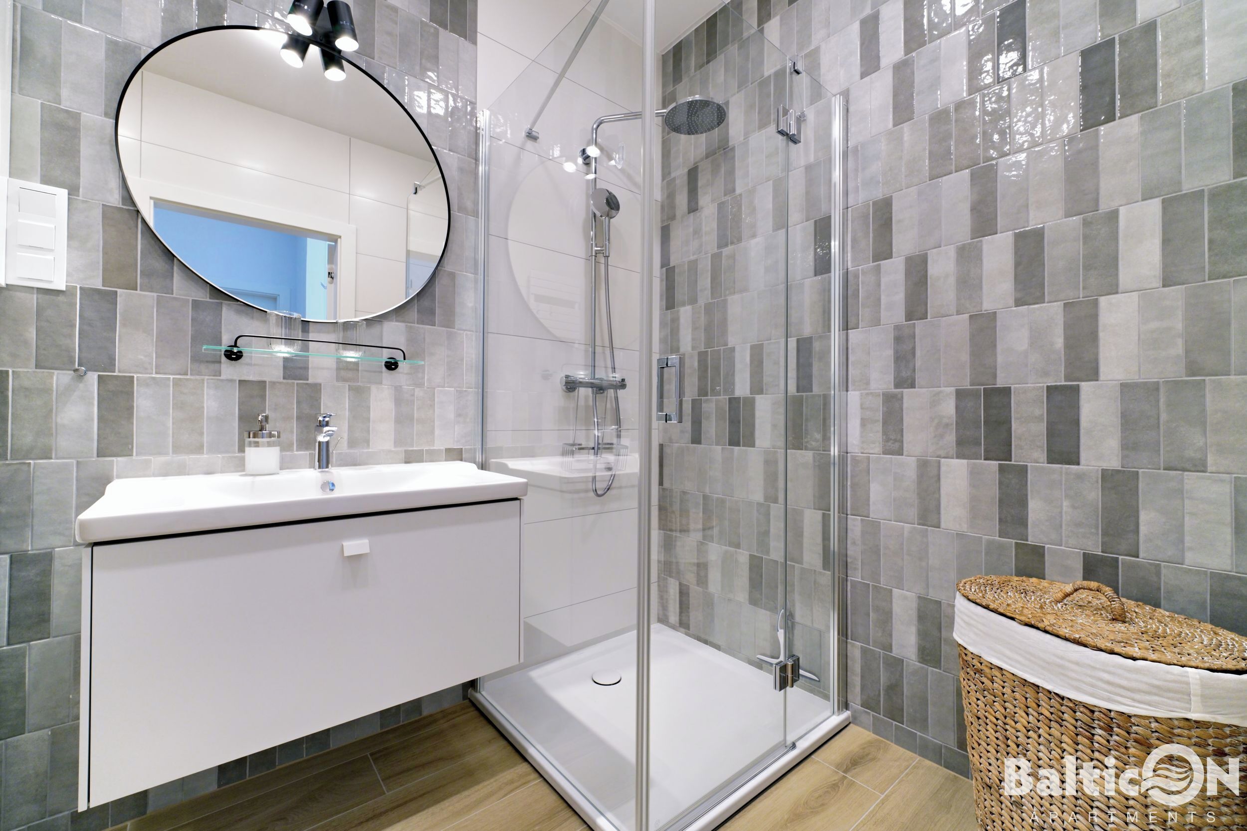 Een moderne badkamer met een glazen douchecabine, een witte wastafel met spiegel en een rieten mand.