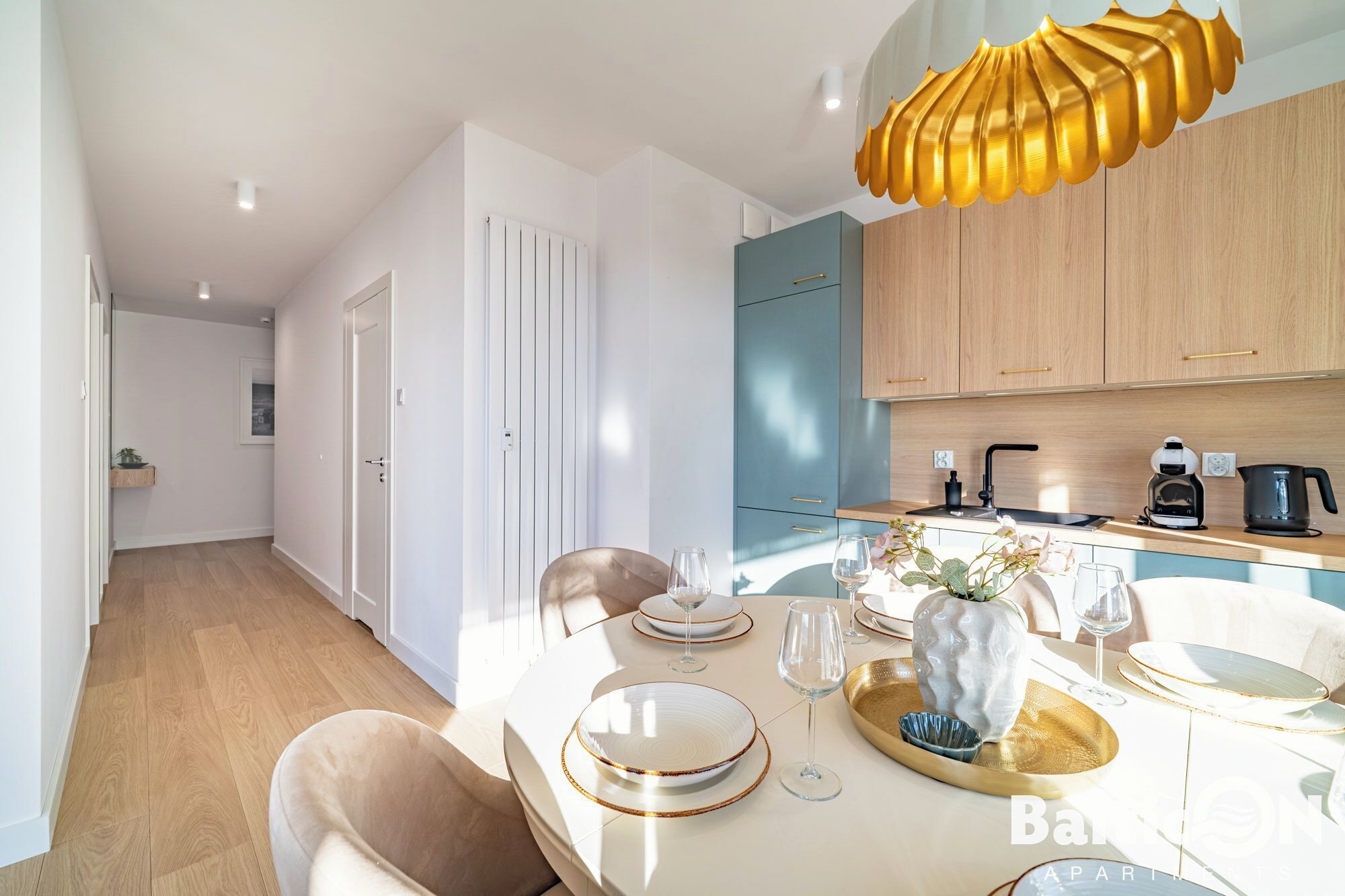 Una cocina moderna con armarios de madera clara, una encimera blanca y una zona de comedor con una mesa blanca para cuatro.