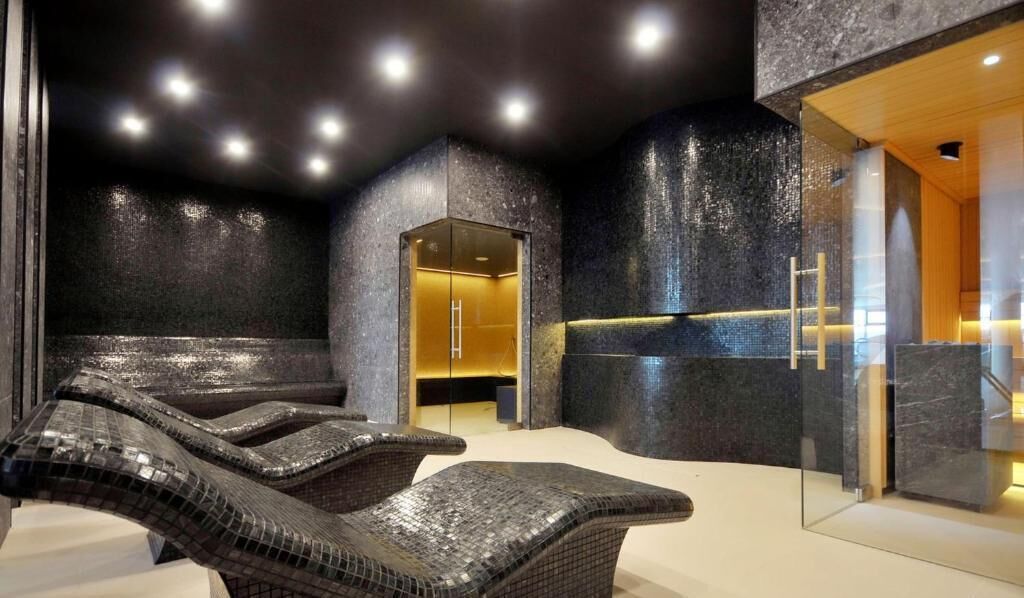 Un espace spa comprenant un coin salon, un fauteuil de massage et un sauna à parois vitrées.