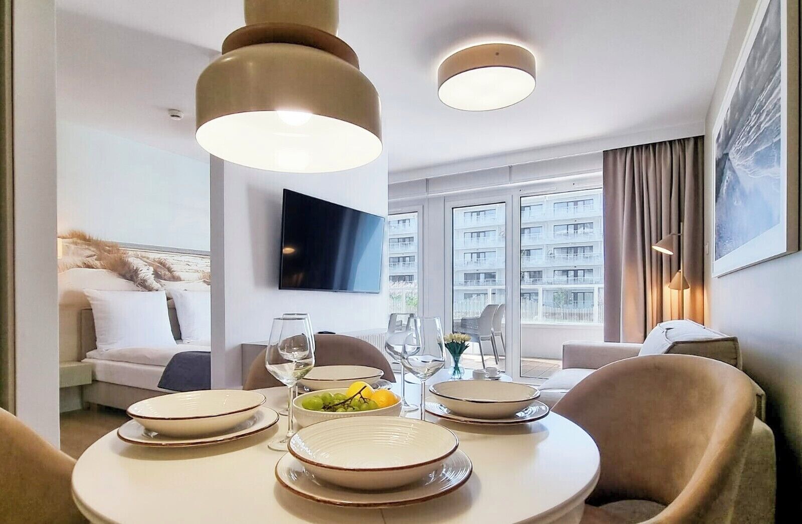 Una habitación de hotel moderna con comedor que incluye una mesa redonda para dos personas, un sofá y un amplio ventanal con vistas a la ciudad.