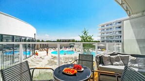 Un balcón con vista a la piscina, mobiliario exterior y una mesa con fruta.