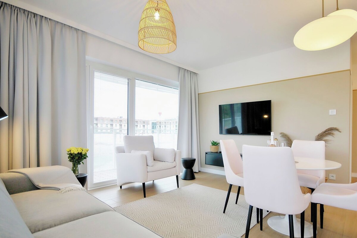 Una sala de estar moderna con un sofá, una mesa de comedor, sillas, ventanas grandes y un televisor de pantalla plana.