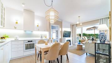 Una cocina moderna con armarios blancos, un comedor con mesa y sillas, y una sala de estar con sofá y televisor.