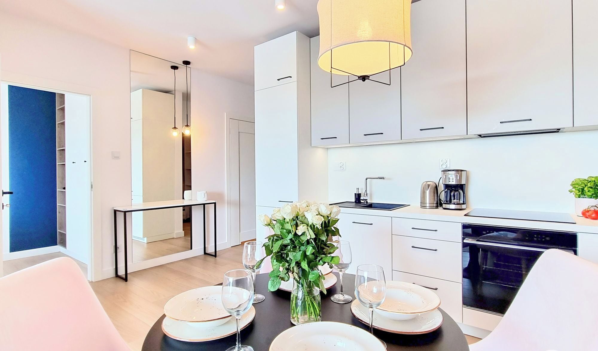 A modern kitchen with white cabinets, a coffee maker, and a dining area with a table set for four.