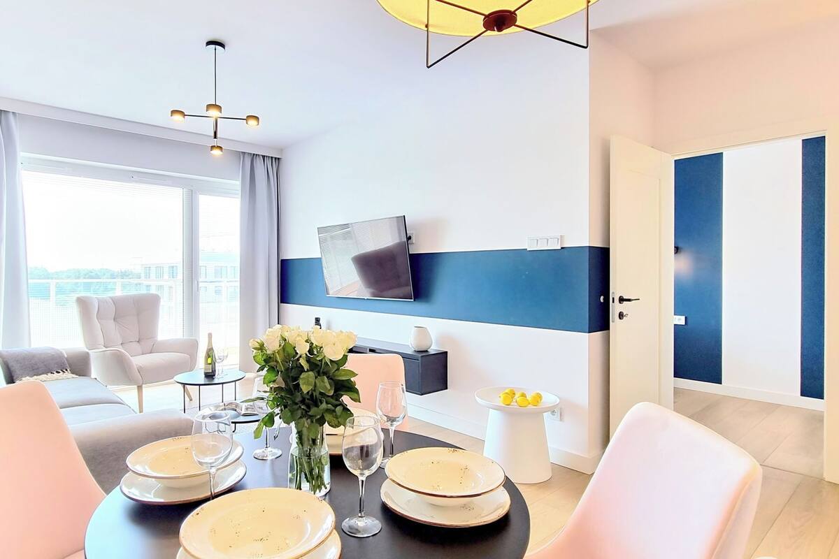 Una camera d'albergo moderna con zona pranzo, televisore a schermo piatto montato a parete e un'ampia finestra con vista sulla città.