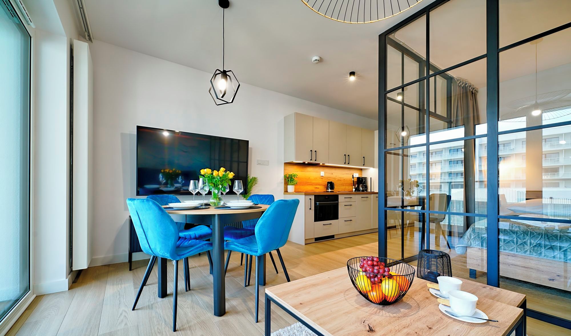Una sala de estar moderna con comedor, cocina y ventanas grandes que ofrecen vista a la ciudad.
