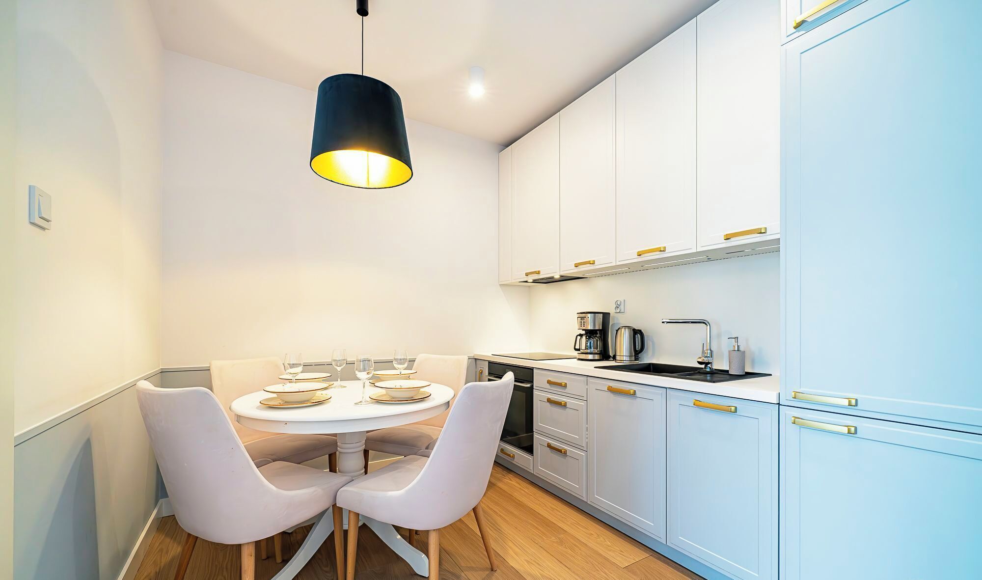 A modern kitchen with white cabinets, a black hanging light, and a dining table with chairs.