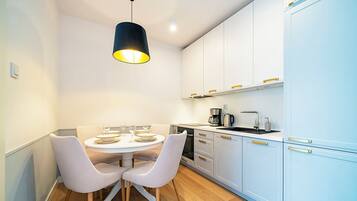 A modern kitchen with white cabinets, a black hanging light, and a dining table with chairs.