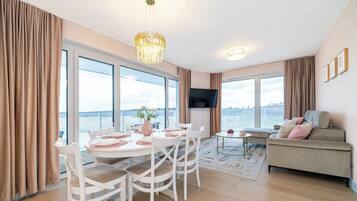 A modern living room with a dining area, large windows, and a flat-screen TV.