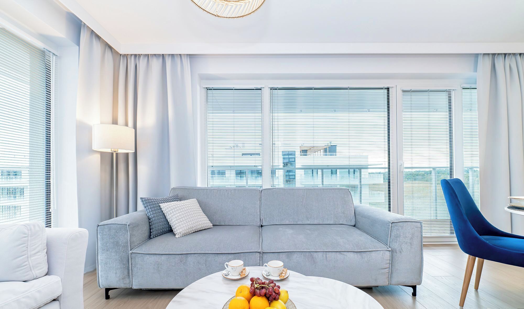 A modern living room with a grey sofa, a round coffee table with fruits and cups, and a blue chair.