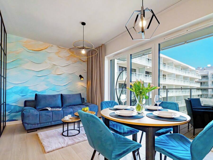 Uma sala de estar moderna com um sofá azul, uma mesa de jantar redonda com cadeiras e vista para um edifício através de grandes janelas.