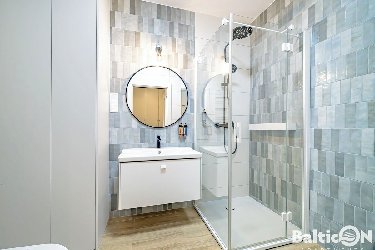 Un baño moderno con cabina de ducha de vidrio, un espejo redondo y un tocador blanco.