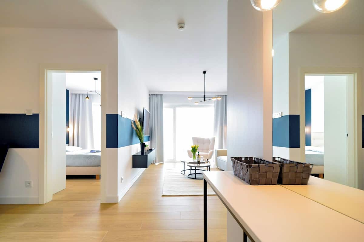 Una moderna camera d'hotel con un letto grande, un'area salotto con divano e poltrone, un tavolo da pranzo e vista sulla città attraverso ampie finestre.