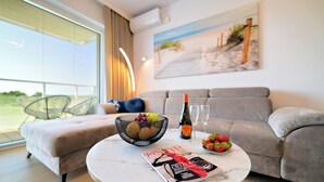 Una sala de estar moderna con un sofá, una mesa de centro redonda, una revista, una botella de vino y un cuenco de fruta.