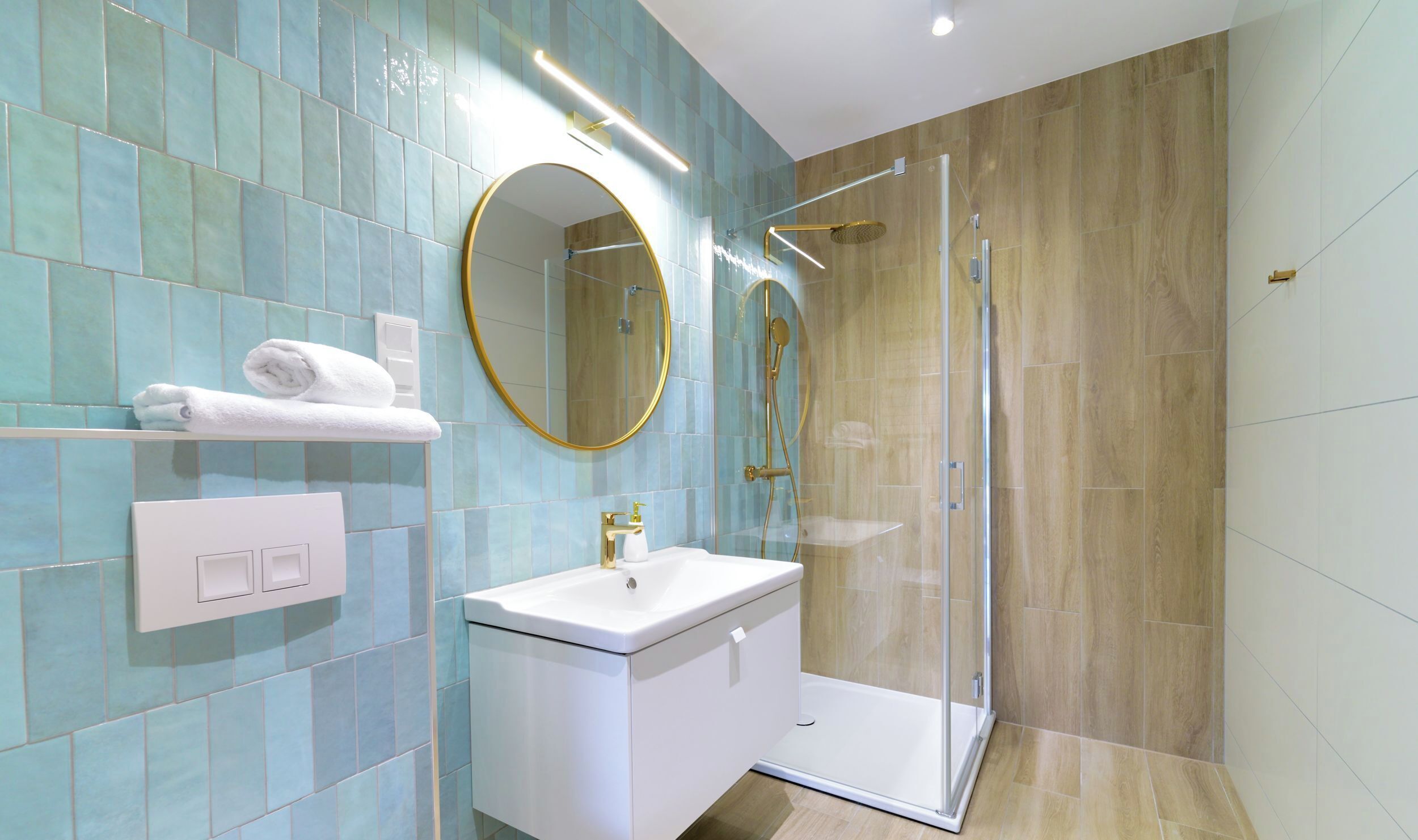 A modern bathroom with a glass-enclosed shower, a white sink, and a mirror with a gold frame.