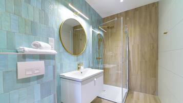 A modern bathroom with a glass-enclosed shower, a white sink, and a mirror with a gold frame.