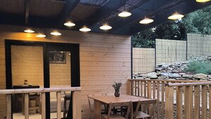 Una terraza de madera con una mesa y sillas, una planta en maceta y un muro de piedra al fondo.