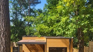 Una cabaña de madera con techo inclinado, rodeada de árboles y un muro de piedra.