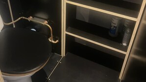 Ein kleines Badezimmer mit Toilette, Ablageflächen für Pflegeprodukte und einer sichtbaren Rohrleitung.