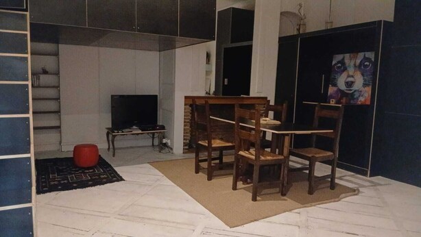 Ein Wohnzimmer mit Fernseher, Holzstühlen, einem kleinen Tisch und einem Gemälde an der Wand.