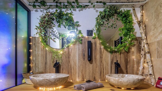 Un baño con dos lavamanos de piedra, paneles de madera en la pared y plantas decorativas.